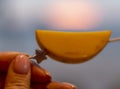 Blurry, unfocused photo. A piece of fruit on a skewer in a woman\'s hand against the sunset