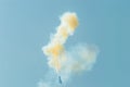 Blurry view of an aerobatic plane leaving a white and yellow smoke trail in the blue sky. Royalty Free Stock Photo