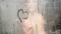 Blurry young woman hand draws heart on bathroom glass shower Royalty Free Stock Photo