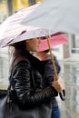 Blurry young woman walking fast under the umbrella on rainy and crowd city street