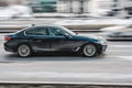 BMW 5 series on the road in motion. Black shiny sedan moving fast. Side view of sedan car rushes along the street