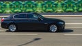 BMW 5 series on the road in motion. Black shiny sedan moving fast. Side view of premium car with blurred background