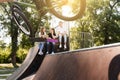 Bmx bicycle rider making tricks and sports kids with skateboard and penny boards are sitting and chatting on background