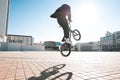 Bmx rider makes a trick in the jump on the street in the background of the city landscape and the sun Royalty Free Stock Photo