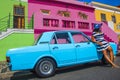 A beautiful African woman in a blue and white striped dress in front of a vintage Ford Cortina and traditional homes of Bo-Kaap, C