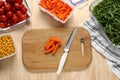 Board with baby carrots, knife and containers with fresh products on wooden table, flat lay. Food storage