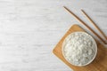 Board with boiled rice in bowl and chopsticks on wooden background, top view Royalty Free Stock Photo