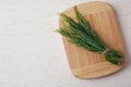 Board with bundle of fresh rosemary twigs on white wooden background. Space for text