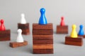 Board game piece on wooden blocks dominating other figures against grey background.
