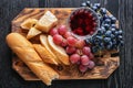 Board with grapes, glass of wine, bread and cheese on dark wooden table Royalty Free Stock Photo