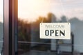 A board hung open in front of the glass door of the coffee shop. The soft light of the morning sun is bright as the background. Royalty Free Stock Photo