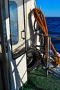 On board old yacht, white ship door with red ropes in the light of sun light in blue sea with foam and splashes