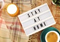 Board with Stay At Home writing, cup of coffee, burning candle and plaid on the wooden background