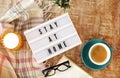 Board with Stay At Home writing, cup of coffee, burning candle and plaid on the wooden background