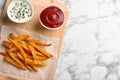 Board with sweet potato fries and sauces on marble background. Space for text Royalty Free Stock Photo