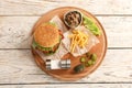 Board with tasty burger, french fries and vegetables on wooden table Royalty Free Stock Photo