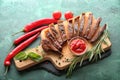 Board with tasty cut steak, herbs and sauce on green background