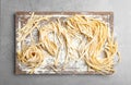 Board with uncooked egg noodles and flour on grey table Royalty Free Stock Photo