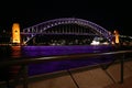 Sydney Harbor Bridge in purple light at night. Glowing water reflection. Embankment promenade. Iconic city waterfront nightscape. Royalty Free Stock Photo