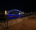 Sydney Harbor Bridge in blue light at night. Glowing water reflection at embankment promenade. Iconic city waterfront nightscape. Royalty Free Stock Photo