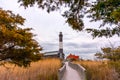 Boardwalk leading to a stone lighthouse framed by tall beach grass and trees. Fire Island