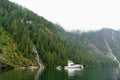 A boat anchored in front of a beautiful waterfall surrounded by rugged forests and mountains in princess Louisa inlet