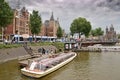 Boat Canal Cruises on a river with Amsterdam Central Station in the background with cloudy sky