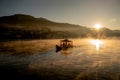 Boat with Chinese roof style sail in big lake with mist cover the surface of water and warm light in early morning Royalty Free Stock Photo