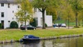A boat on the city lake, autumn, along with cars parked on the street, white residential buildings and green grass Royalty Free Stock Photo