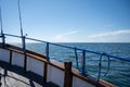 A boat deck with a blue rail and fishing rods. Background with a clear blue sky and blue ocean Royalty Free Stock Photo