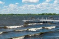 Boat dock with benches on a lake with waves rolling in and city buildings