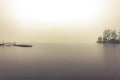 Boat dock and a lonely island in fog that sank low on the water of a large river at sunrise Royalty Free Stock Photo