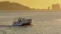 Boat in front of silhouette of hill of Almada and silo`s against golden sunset sky in the port of Lisbon