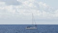 Boat with furled sails sailing across blue sea under cloudy sky, recreation