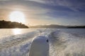 Boat glides on ocean at sunrise, reflecting sunlight and creating wake. Royalty Free Stock Photo