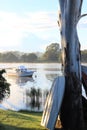 Boat leaning against large gum tree with another boat on the river in the bacground Royalty Free Stock Photo