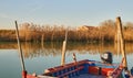 Boat moored in the canal of the lagoon of Caorle in Venice, Italy, with reeds reflected in the sea and a house in the background