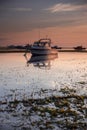 Boat in the ocean. Sunrise view. Low tide. Sunlight on horizon line. Cloudy sky. Water reflection. Soft focus. Slow shutter speed Royalty Free Stock Photo