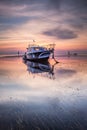 Boat in the ocean. Sunrise view. Low tide. Sunlight on horizon line. Cloudy sky. Water reflection. Soft focus. Slow shutter speed Royalty Free Stock Photo