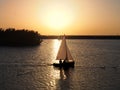 boat sailing on a lake across the path of a golden sunset with unidentifiable people in silhouette and swans swimming in the Royalty Free Stock Photo