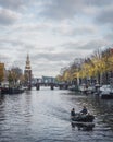 A boat sails along a can in Amsterdam towards the Montelbaanstoren tower on an autumn day.