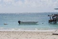 Boat tied to deck in shimmering water on sandy beach, with wispy blue sky in background