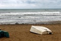 A boat is upside down on the sand of the beach with a sea background in a cloudy day