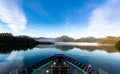 Boat view of landscape with hills and trees reflected in lake water under blue sky with white clouds Royalty Free Stock Photo