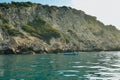 A boat in the water behind cliffs