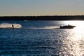A boat and water skier silhouetted against a blue lake Royalty Free Stock Photo