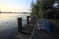 Boat on a wooden pier by the lakeshore next to reeds at sunset