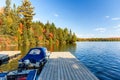 Boats tied up to wooden jetty on a lake with forested shores at the peak of fall foliage on a sunny day Royalty Free Stock Photo