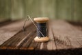 a bobbin with a black thread and a needle stuck into it stands on a wooden table