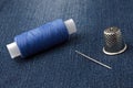 A bobbin of thread with a needle and a thimble. on denim background. close-up Royalty Free Stock Photo